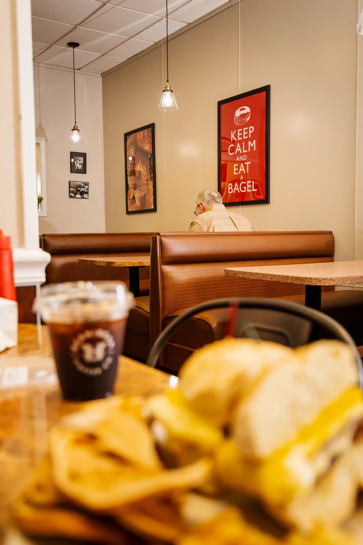 Restaurant interior with a table featuring bagels and a drink, framed poster on the wall.