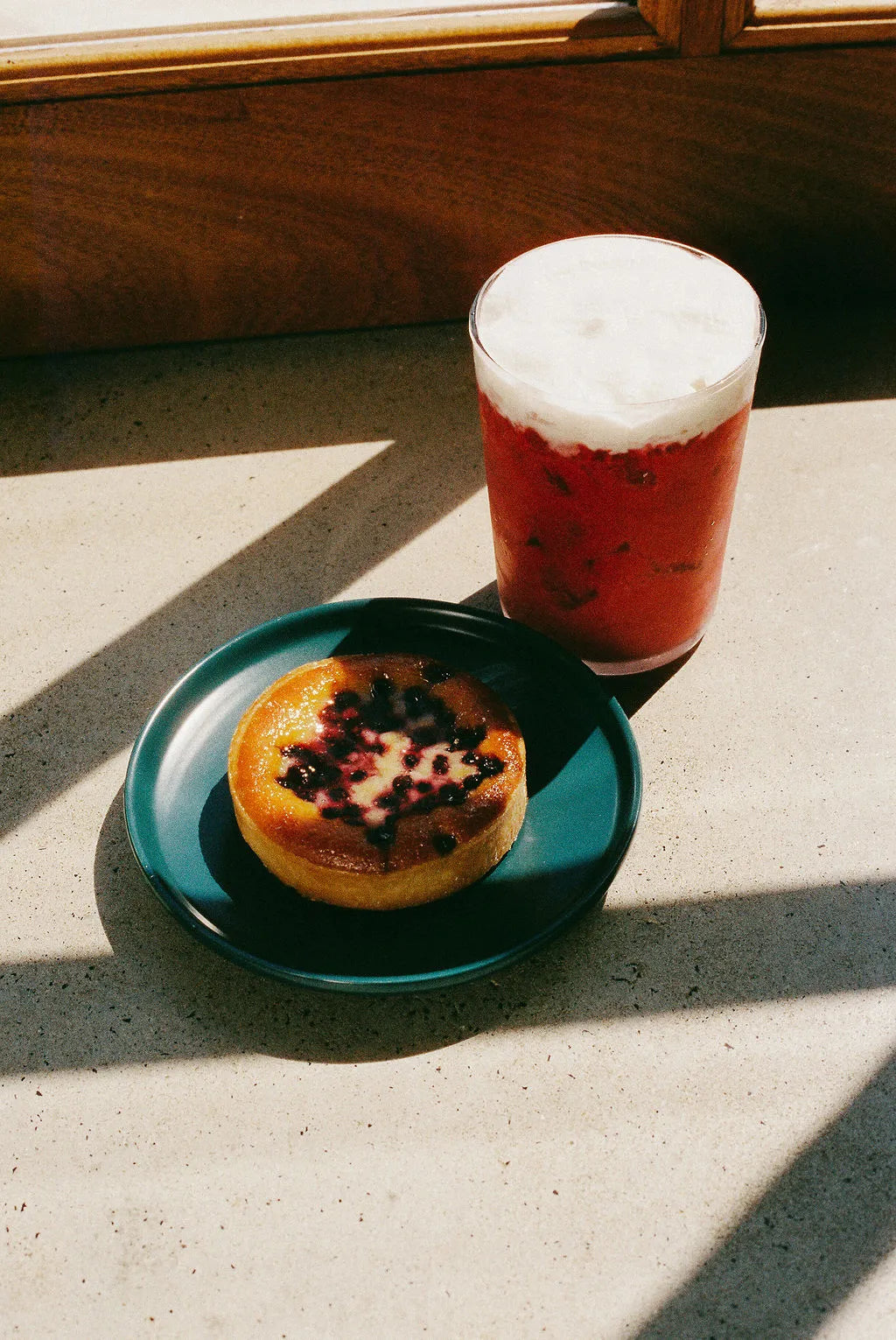 Pastry with berries on a green plate next to a glass of red beverage with white foam on a concrete surface.