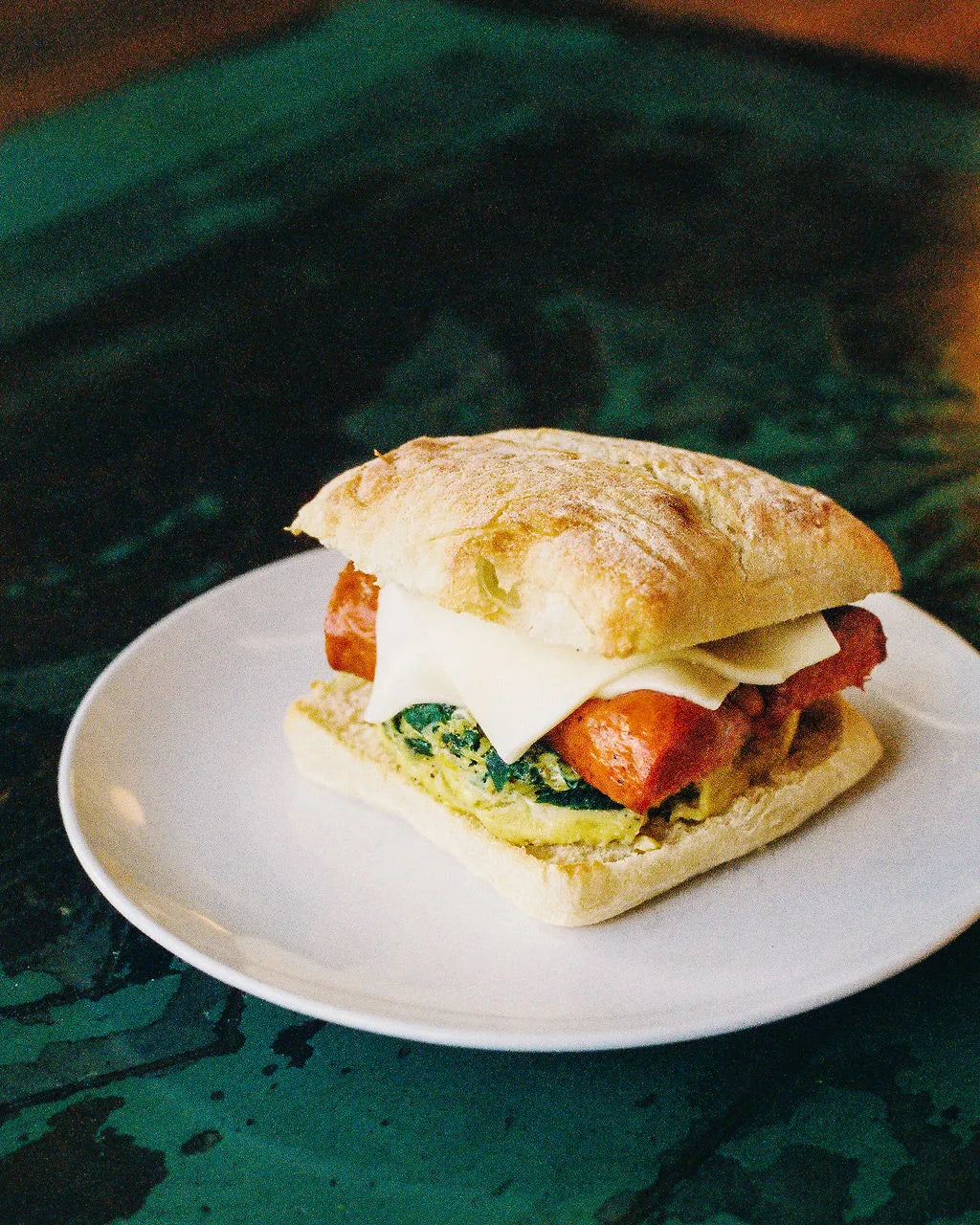 Sandwich with chorizo, egg, and cheese on a white plate with a green textured background