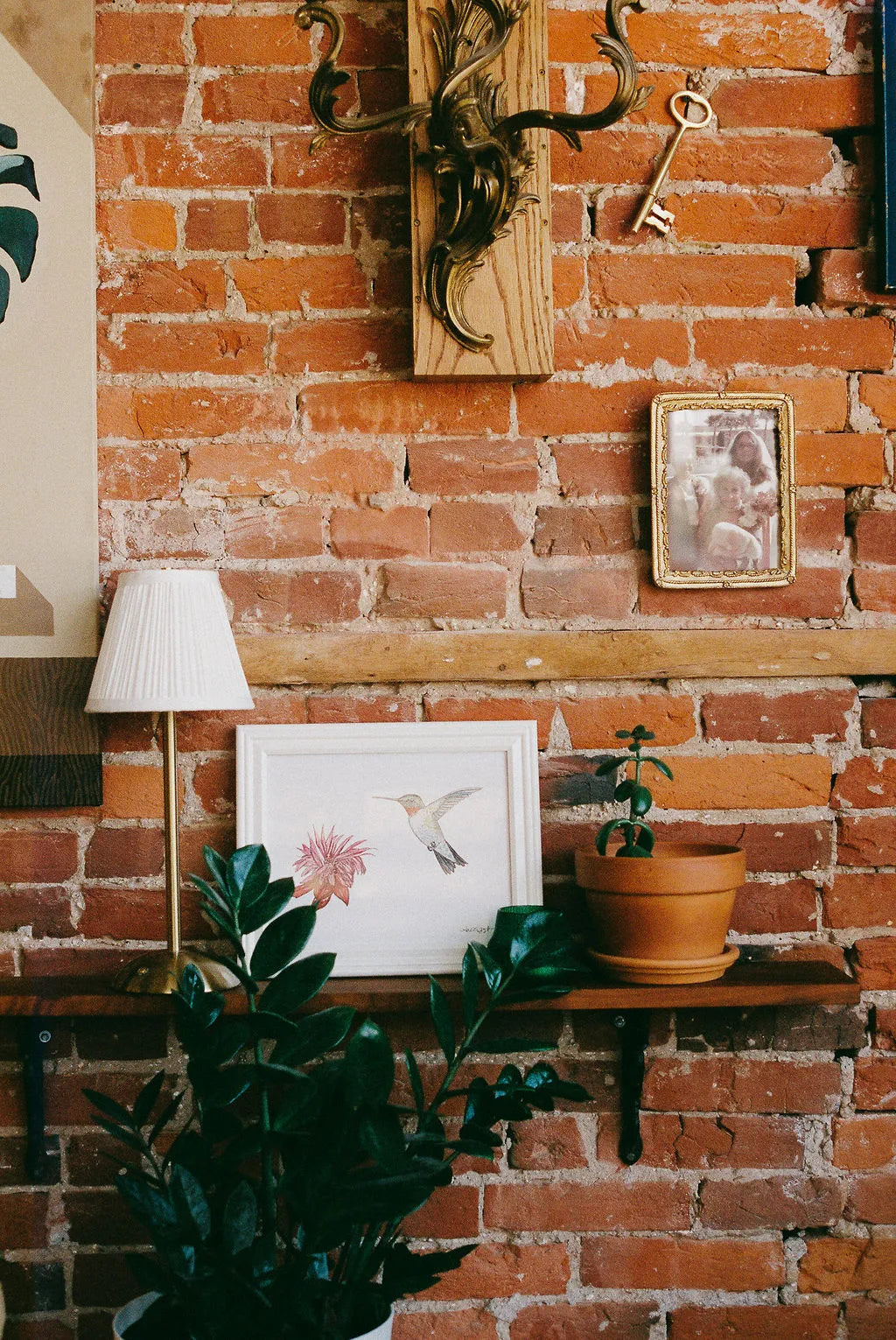 Brick wall with wooden shelf, lamp, plant, and framed picture