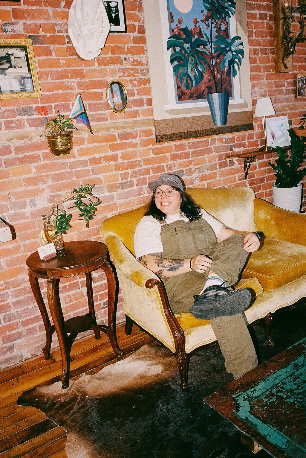 Person sitting on a yellow couch in a cozy room with brick walls and decorative items.