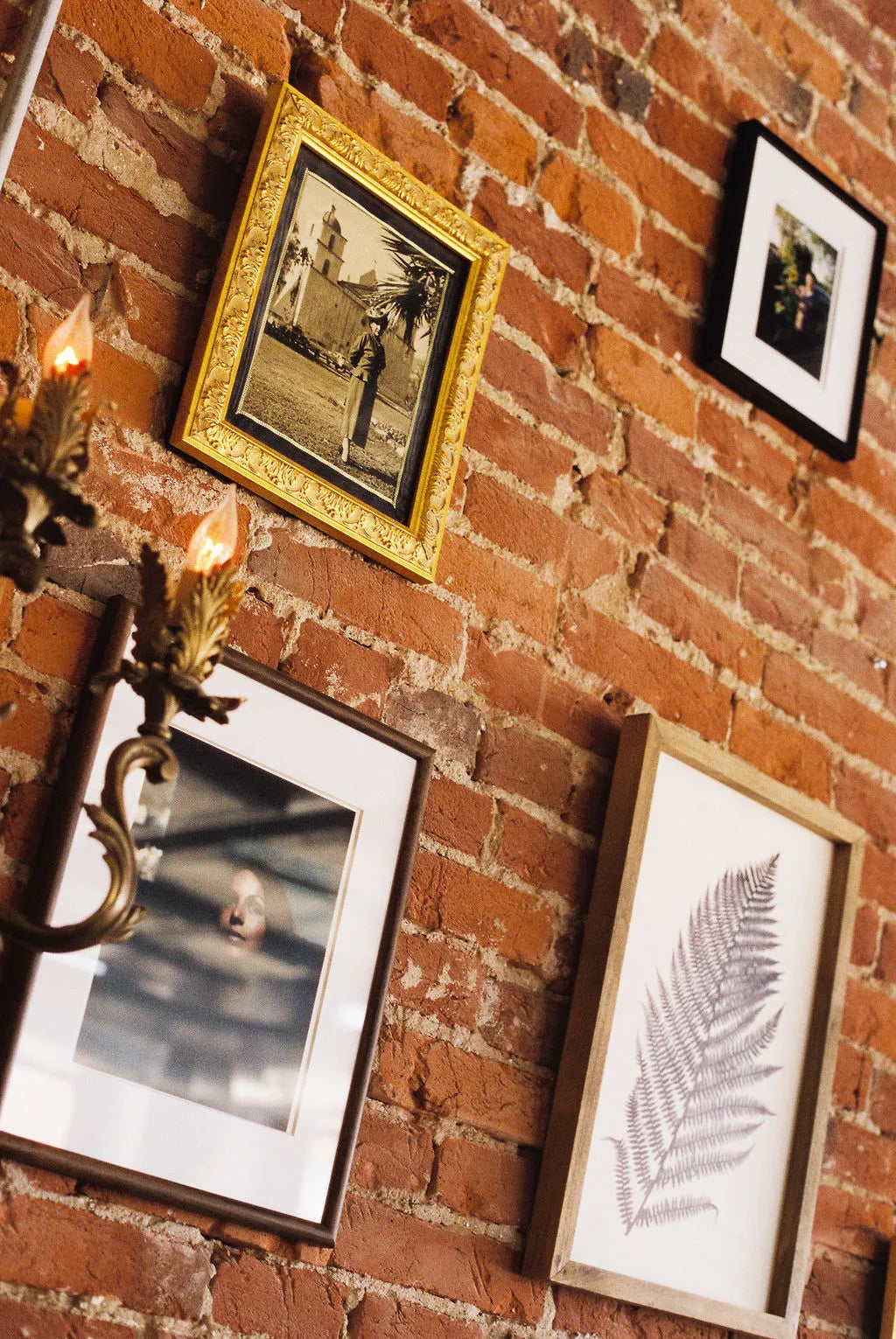 Framed pictures on a brick wall with a chandelier.