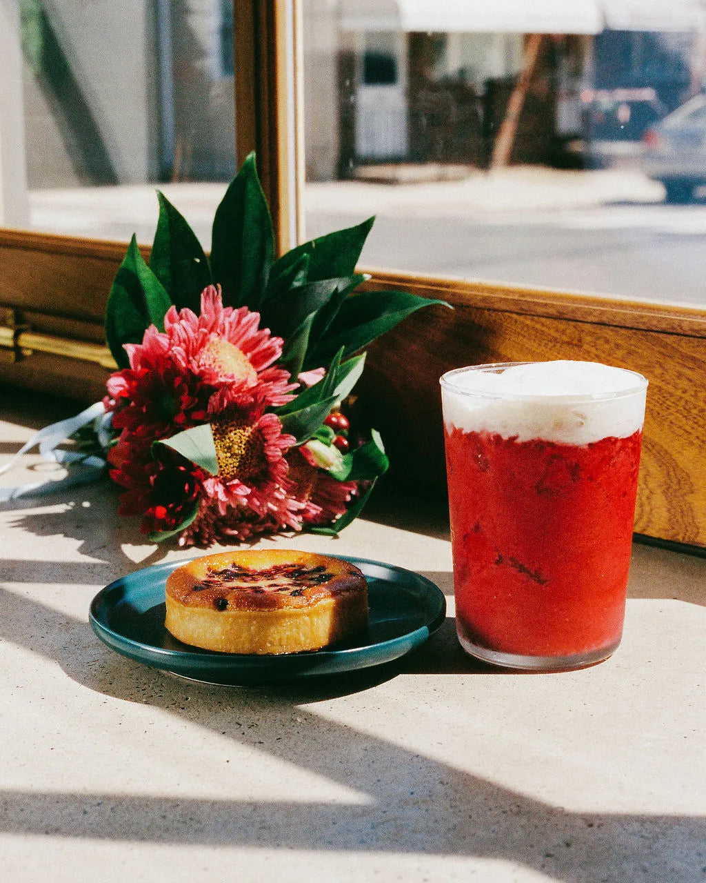 Red drink with foam, pastry, and flowers on a windowsill
