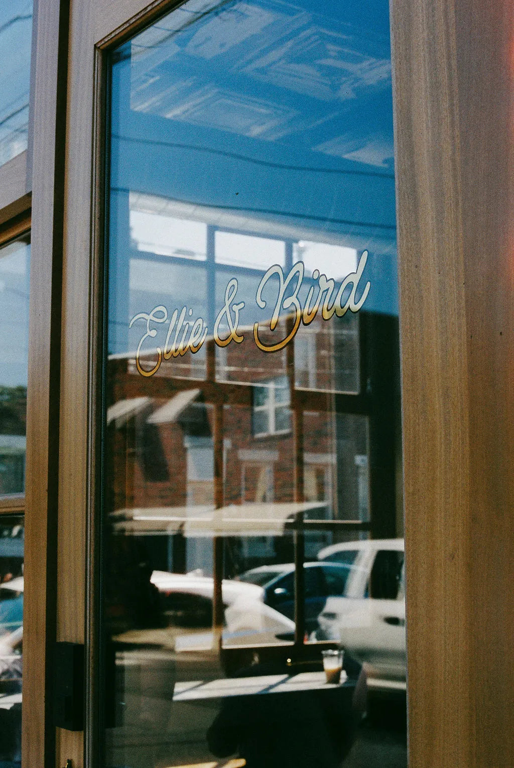 Glass door with 'Elle & Bird' gold lettering on the glass, reflections of cars and building visible