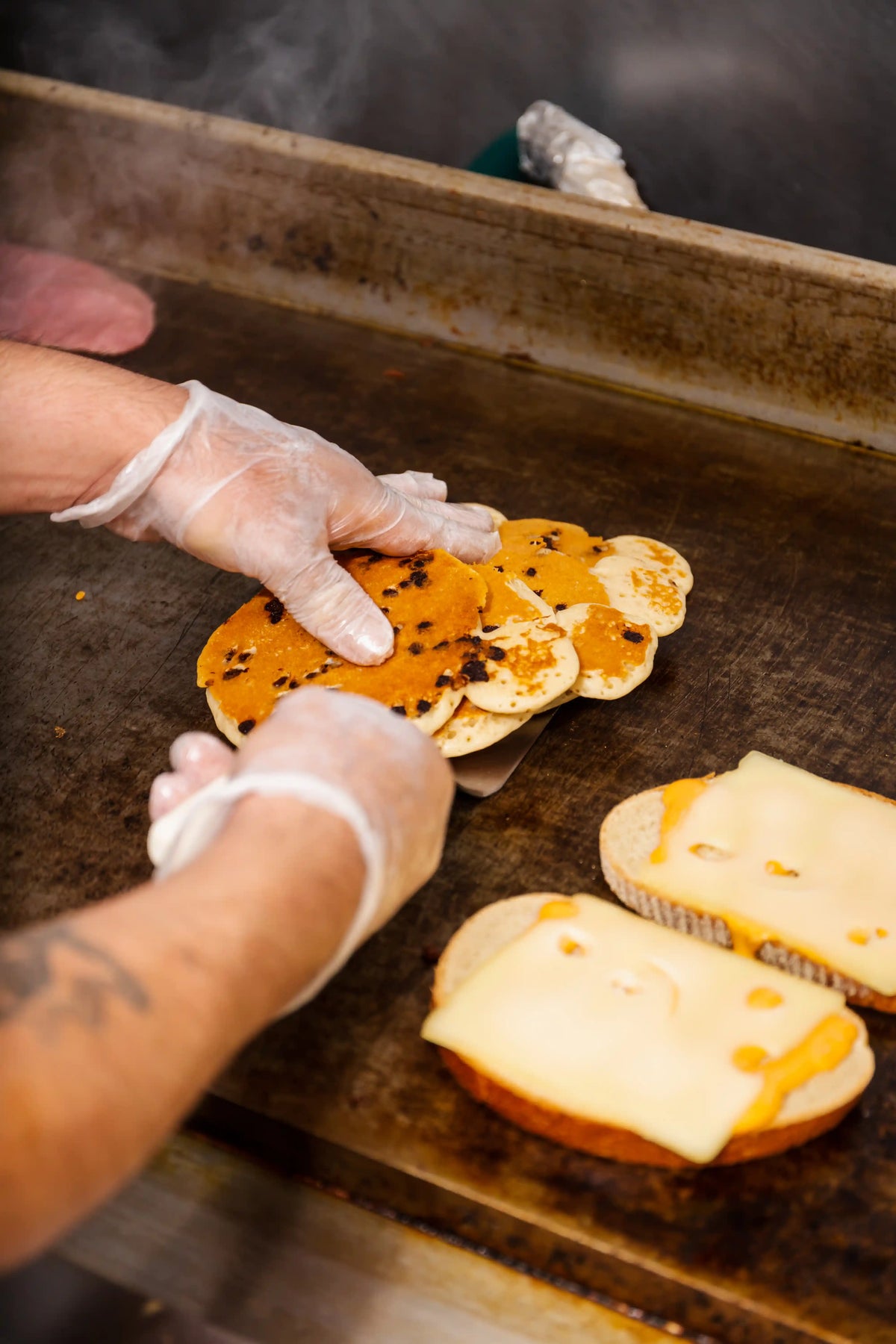 Person preparing sandwiches on a grill with cheese and bread.