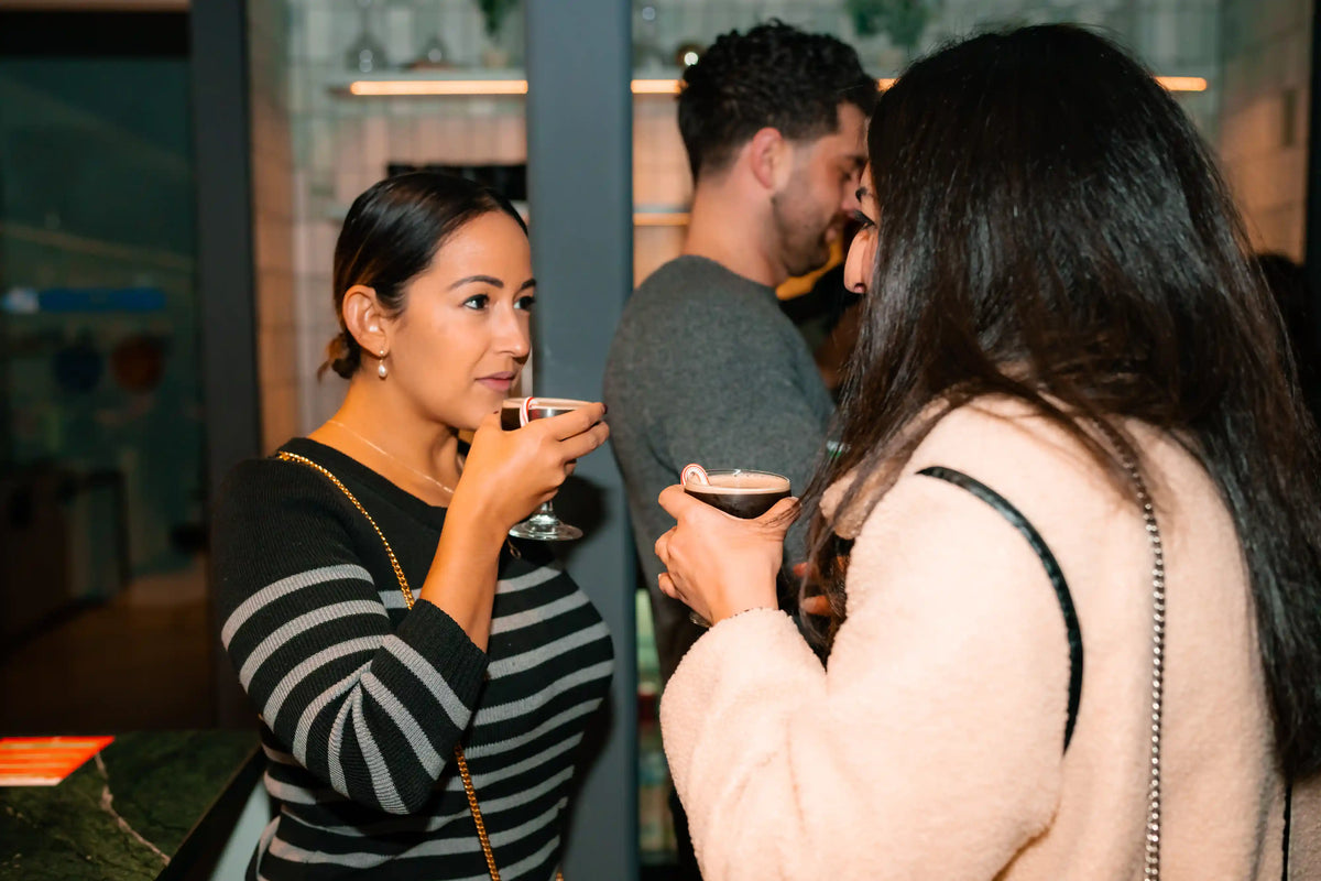 Two women socializing at aBond Collective event, holding Bean2Bean espresso drinks.