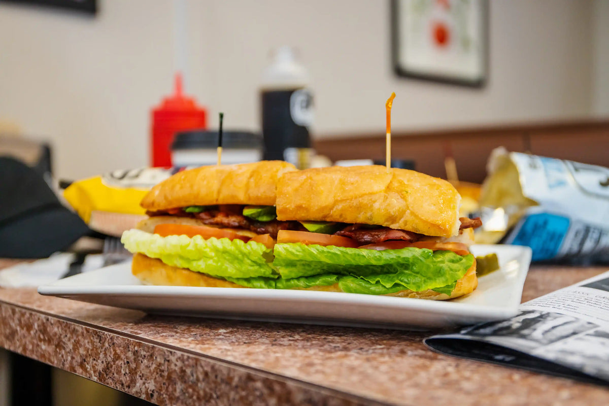 Large sandwich on a plate with condiments in the background
