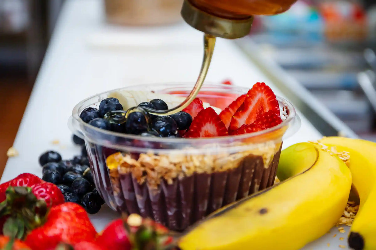 Fruit cup with berries and a drizzle of honey on a white surface