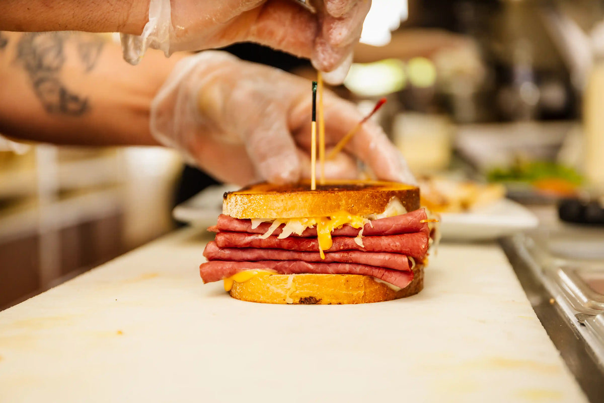 Person assembling a sandwich with deli meats and cheese in a kitchen setting.