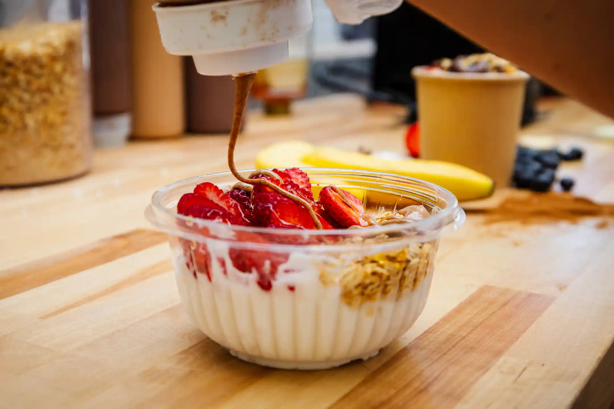 Yogurt bowl with granola, strawberries, and a banana on a wooden table.