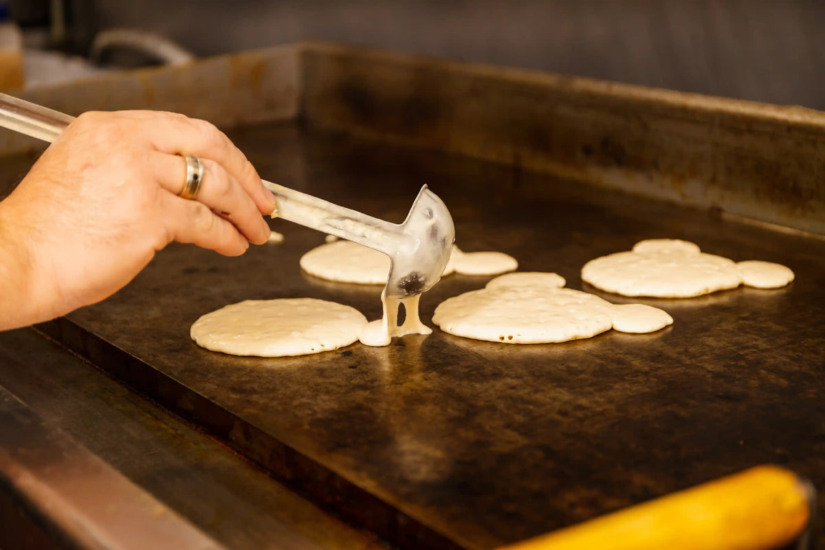 Person flipping pancakes on a griddle with a spatula