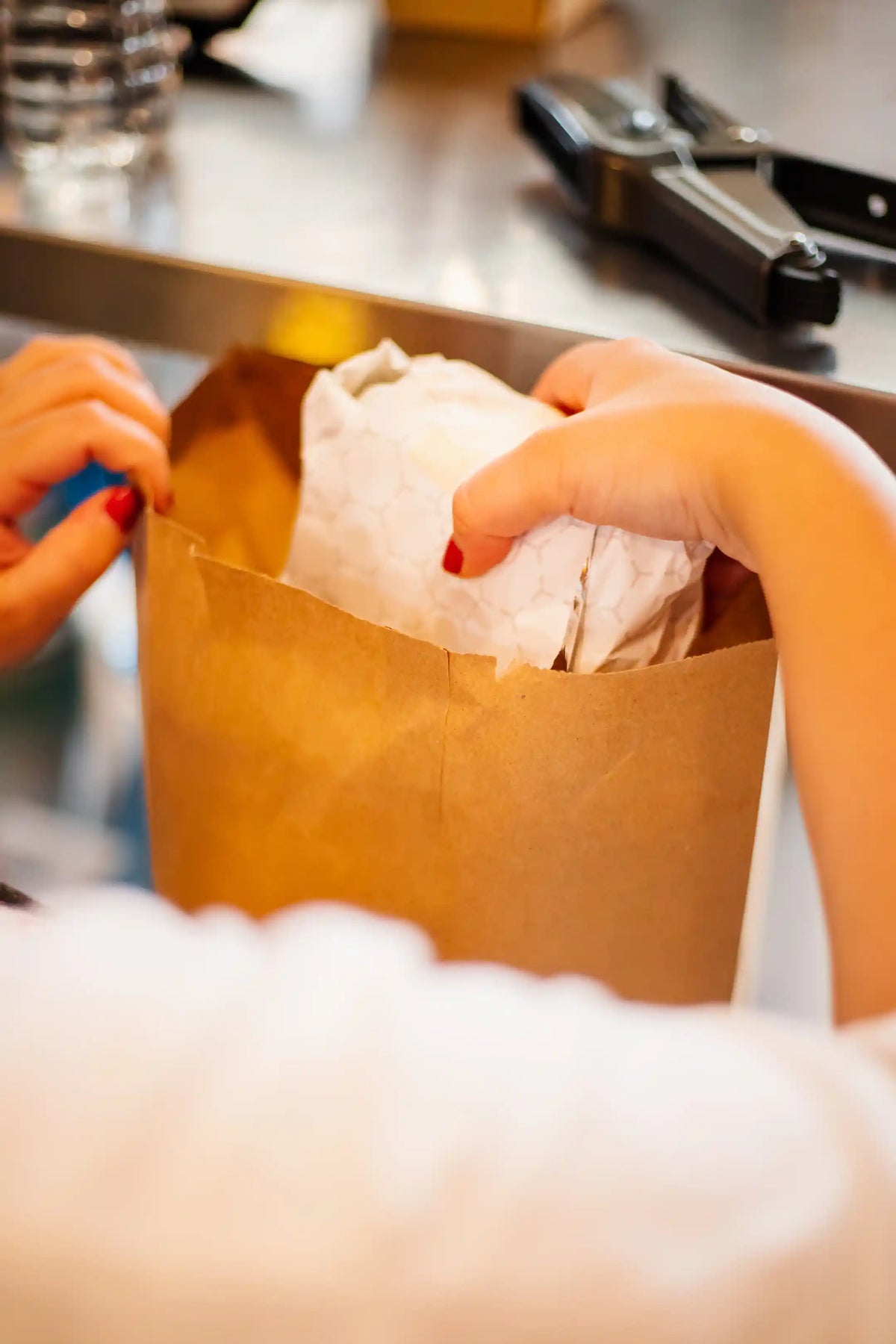 Person insertning a wrapped sandwich into a brown paper bag