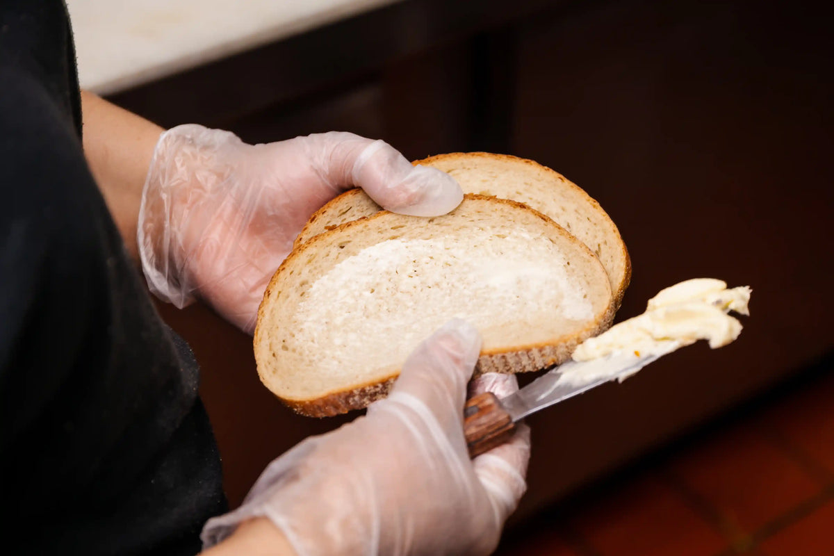 Person spreading butter on a slice of bread with a knife, wearing gloves.