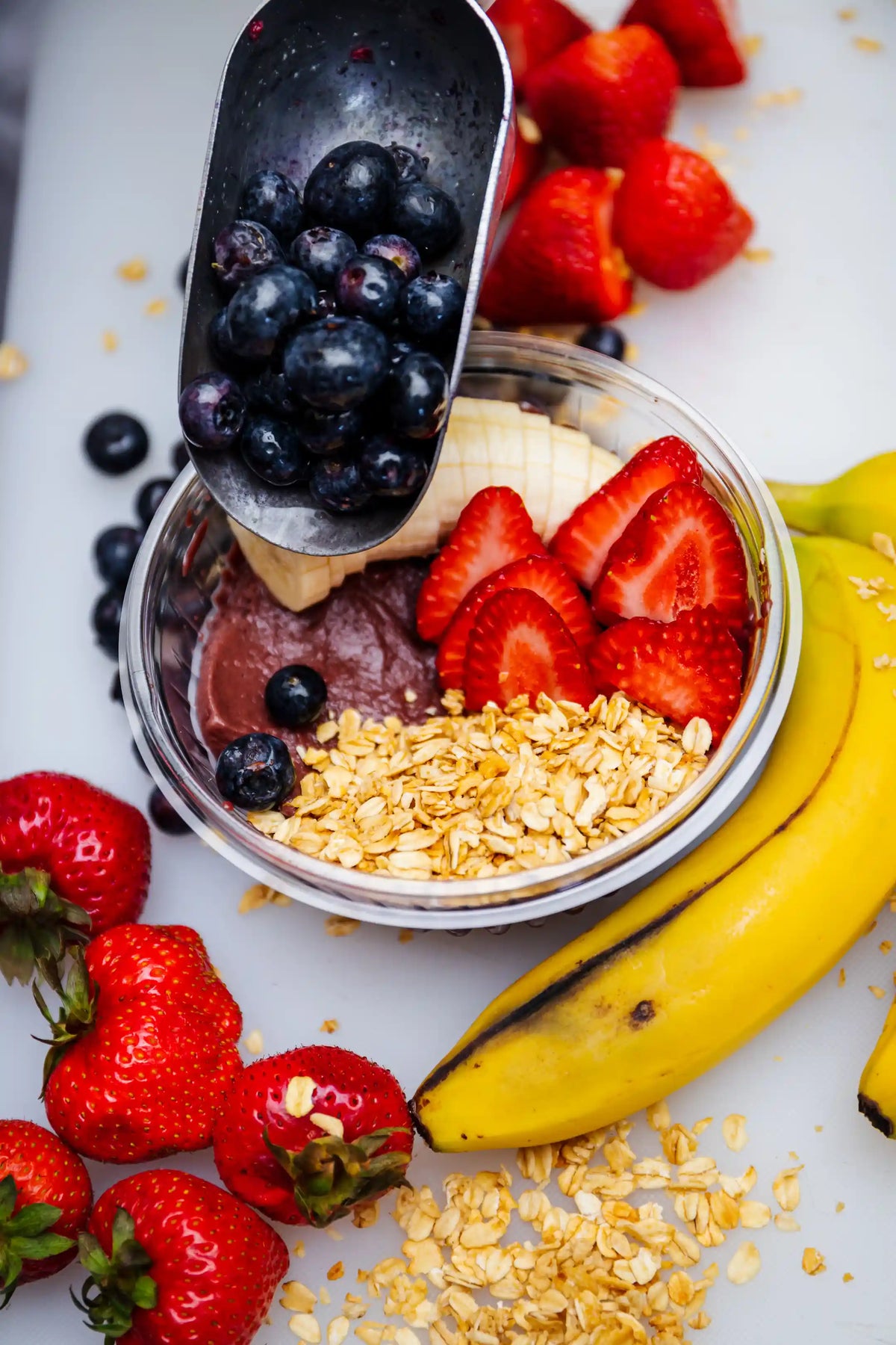 Chocolate yogurt bowl with granola, berries, and a scoop of blueberries on a white background