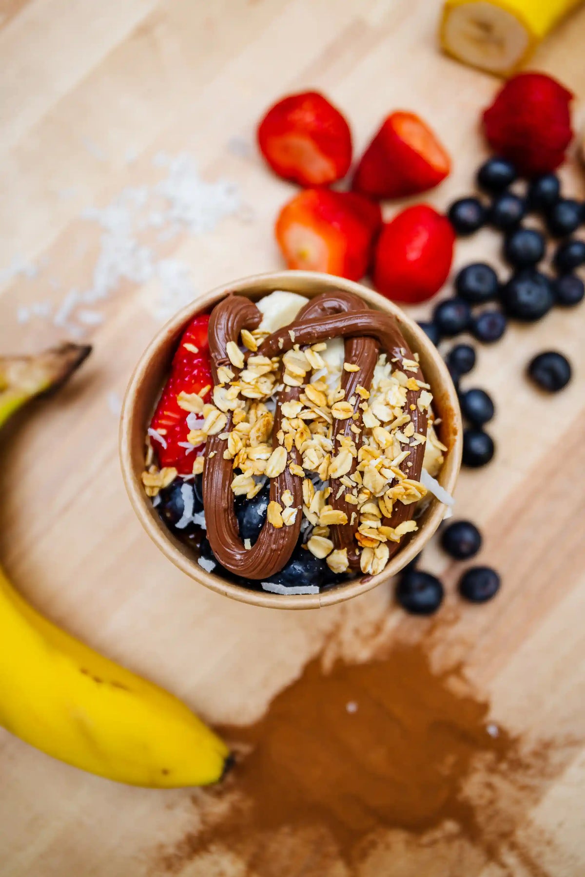 Fruit bowl with chocolate drizzle and granola on a wooden surface