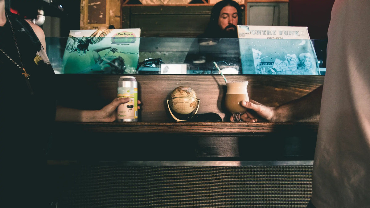 Two people at a DJ Booth bar counter with drinks and records in the background