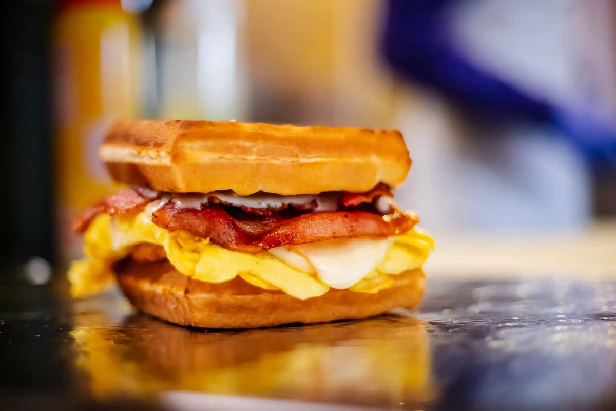 Close-up of a sandwich with bacon, egg, and cheese on a metal surface.