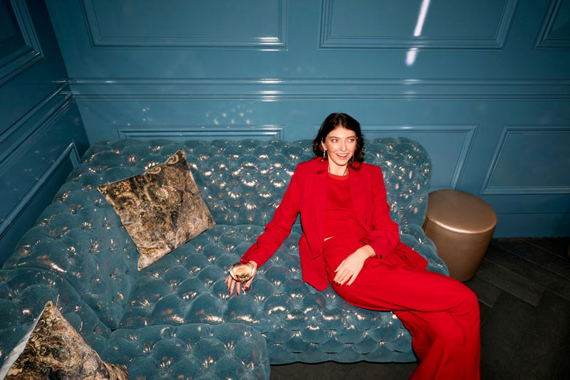 Woman in a red outfit sitting on a textured blue sofa against a blue paneled wall.